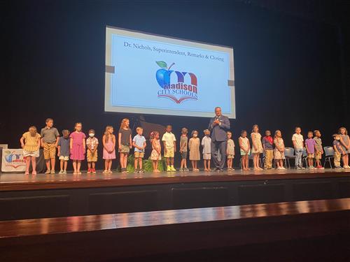 Dr. Nichols with about two dozen elementary kids behind him on stage